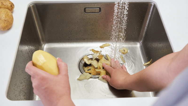 Potato peels being pushed down a sink garbage disposal.