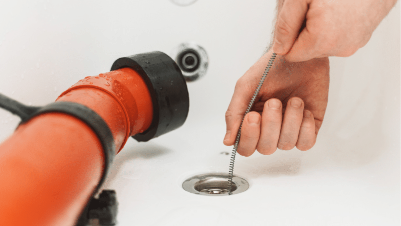 A man using a drain snake to clean a bathtub drain.